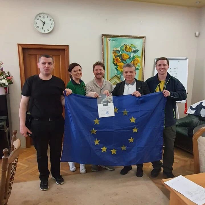 A group gathered indoors holding a European flag during the work in Ukraine